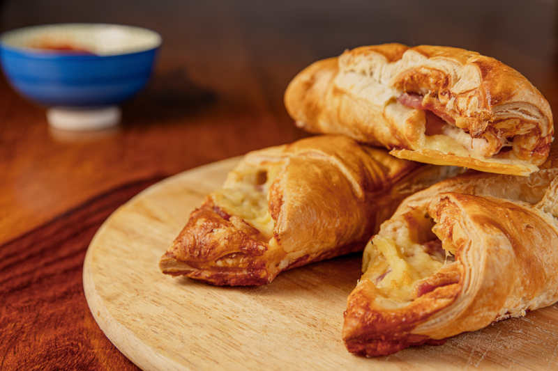 Hot Bacon and melting cheese in a golden toasted sliced baguette on a wooden server with a blue bowl of sauce in the background Tobermory Stores hot and cold takeaway food all day